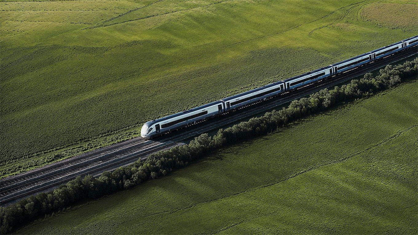 Aerial view of a white high-speed train traveling through green fields.